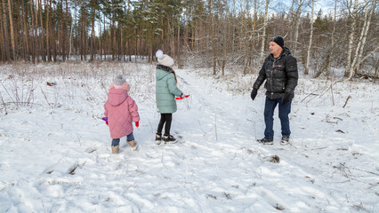 Little girls play with snow with her grandfather in winter forest
