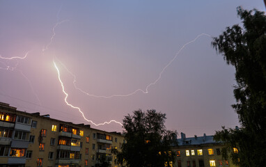 Bright lightning across the sky against the backdrop of houses with windows with lights on.