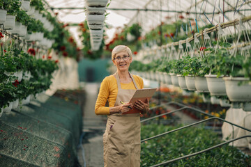Portrait of old florist with clipboard in hothouse smiling at camera.