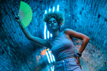 Young woman holding green hand fan dancing under blue neon lights