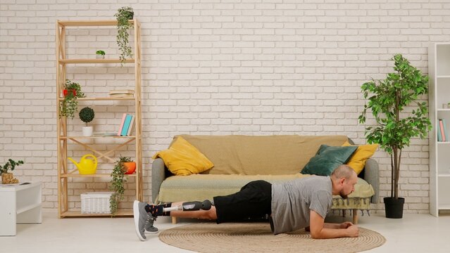 A man with a prosthetic leg in a cozy living room doing the plank exercise lying on the floor, rehabilitation, healthy living.