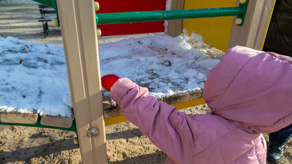 Girl wearing warm clothes playing on the playground in the park in winter