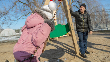 Grandfather playing with his granddaughter on the playground in the park in winter