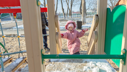 Little girl playing on the playground in the park in snow winter