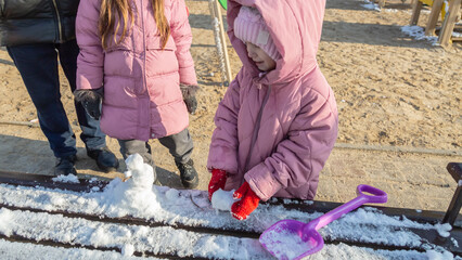 Grandfather with granddaughters making a little snowman in sunny winter day