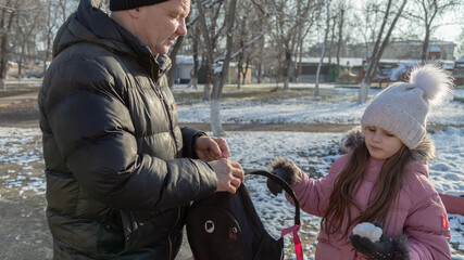 Grandfather walks with his granddaughter after school in the park in winter