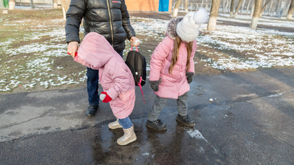 Grandfather walks with his granddaughters after school in the park in sunny winter day