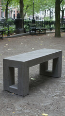 Modern concrete park bench in urban setting, leafy background