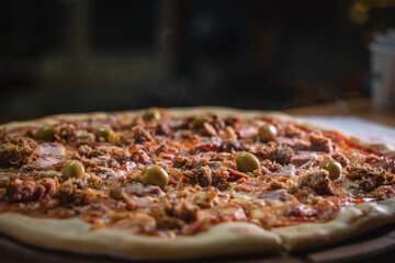 Delicious pizza topped with green olives on wooden platter.