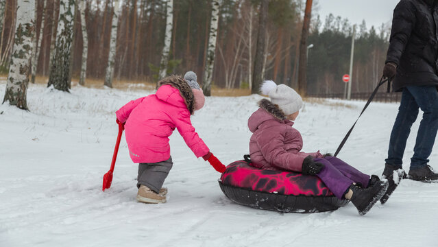 Father and daughters ride downhill on a Snow tubing in the park on the winter holidays