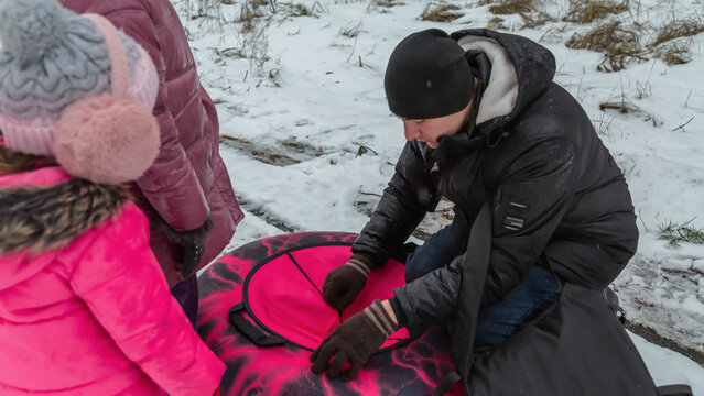 Father and daughters ride downhill on a Snow tubing in the park on the winter holidays