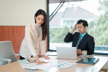 Determined Asian businesswoman explaining data analysis to a male colleague in a modern office.