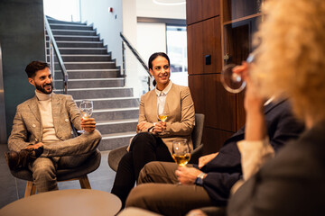 Obraz premium Group of business people sitting in hotel lobby chatting and drinking wine.