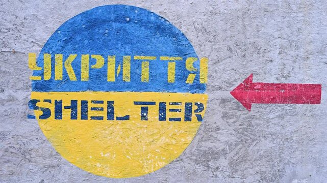 A painted sign on the concrete surface of a ground-based shelter in Ukrainian and English, indicating the entrance direction in Kramatorsk, Ukraine.