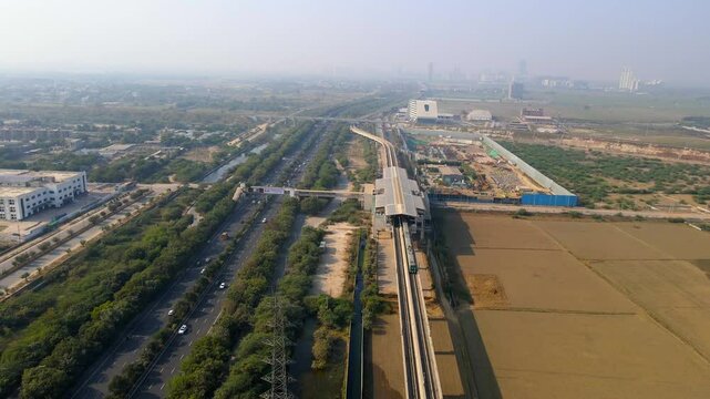 Aerial drone shot capturing Noida metro train along the expressway and farm land