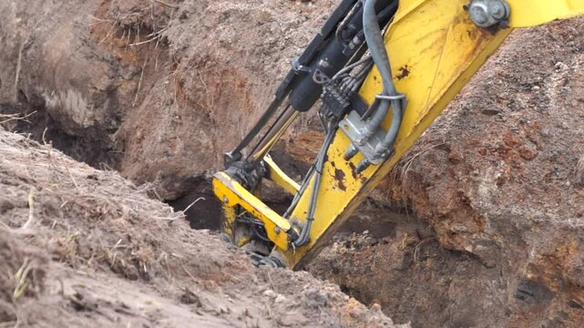 Yellow excavator jib working on digging a ground trench in winter to build extra ground and work as detourant for a beaver dam