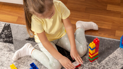 Little girl playing with colorful toy blocks in room at home.