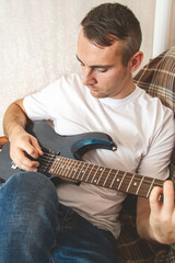 Obraz premium Musical hobby. Guitar skill. Man sitting on sofa playing string instrument enjoying learning chords in living room interior at home