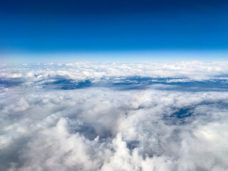 Expansive aerial view of white clouds stretching to the horizon under a deep blue sky. The high-altitude perspective captures the beauty of air travel and nature.
