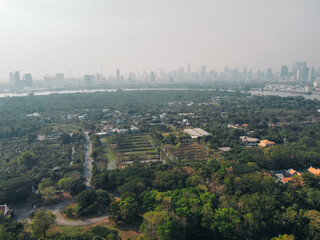 Obraz premium Aerial view of Bangkok urban skyline towering over green cultivated land, forest, and the Chao Phraya River, drone view from Bang Krachao, a green lung near the metropolis, Thailand
