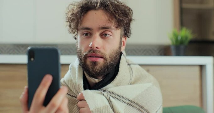 Man with running nose, caughing having video call with doctor while staying at home. Patient video conferencing with general practitioner on smartphone.