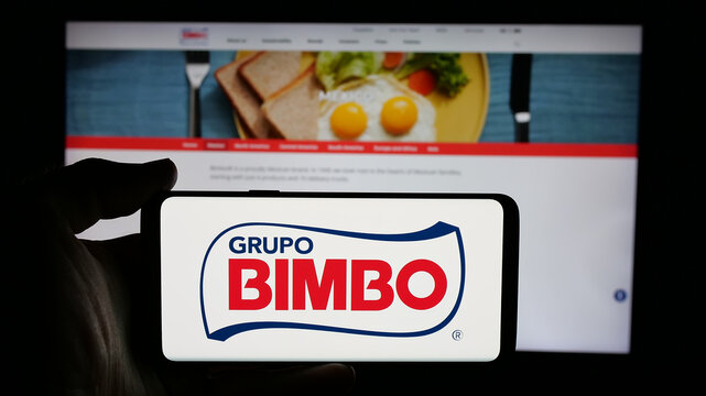 Stuttgart, Germany - 01-28-2025: Person holding cellphone with logo of Mexican food company Grupo Bimbo SAB de CV on screen in front of business webpage. Focus on phone display.