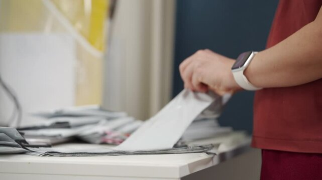 person in a red shirt is seen packing small bags, likely for orders from their online store. They are sitting at a white table with a stack of grey bags already prepped for packaging.
