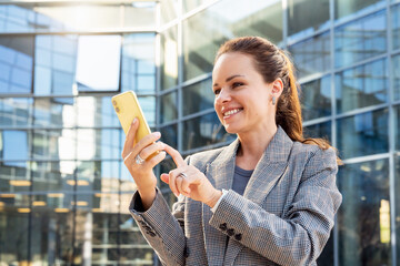 businesswoman sends a message on her smartphone and smiling while standing on city street