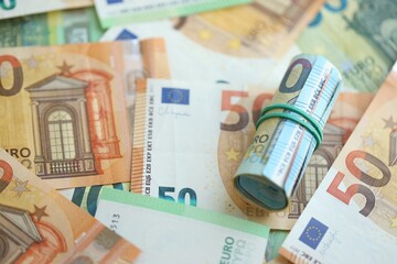 Roll of twenty euro currency bills lies on big amount of hundred and fifty euro banknotes