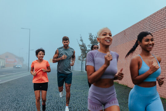 Group of athletes running together on foggy city street