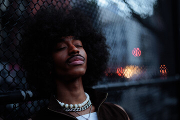 Young man with afro hairstyle is posing near chain link fence