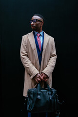 Elegant businessman waiting with briefcase by black wall