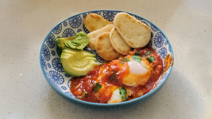 A Plate of tomato and egg shakshuka with avocado and mini naan bread, healthy food