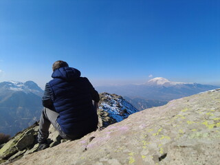 A tourist rests on a mountain peak looking at the beautiful scenery.
