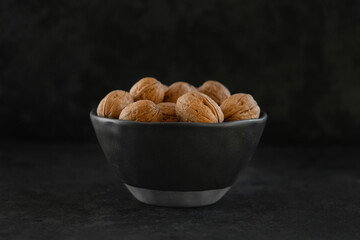 macro photo of walnuts in shell lying in a black ceramic bowl on a dark textured background