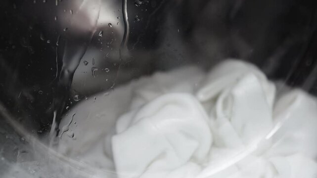 A washing machine filled with white laundry, in action. Concept: utilizing modern technology and cleaning services to simplify household chores and maintain order.