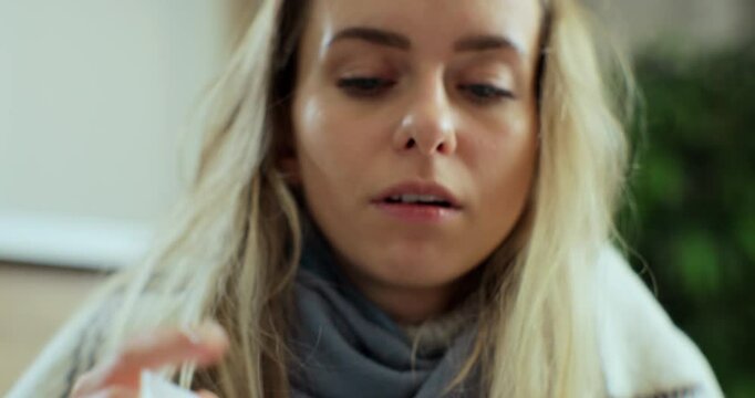 Close up of the young sick woman in the warm scarf and a plaid blowing her nose in the napkin as she having a cold.