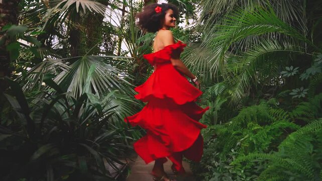 young adult girl happy African woman have fun. red dress black hair perfect skin, sexy fashion model walking dancing spinning enjoying tropical nature forest green palm tree jungle, silk skirt fly 4k