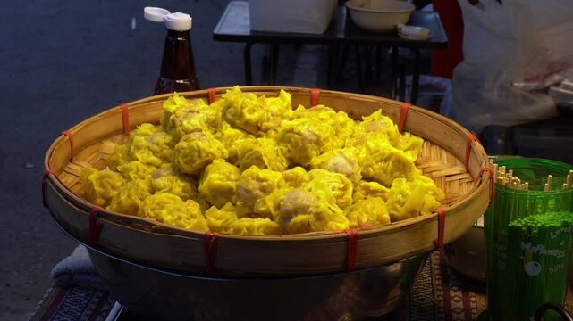 Close-up of freshly steamed Kanom Jeeb dumplings in bamboo steamers, showcasing their delicate golden wrappers and glistening texture as they cook in hot steam - Thailand street food dim sum dumplings