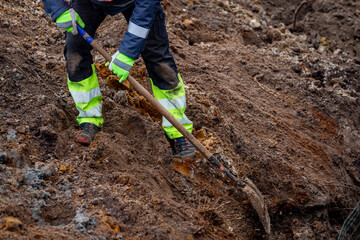 Naklejka premium Man professional construction road digger worker to digging a trench of earth ground. Road construction digging works in professional construction worker clothes