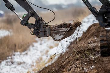 Mini excavator leveling earth moving project works with dirt and snow mixing together in bucket. White excavator working on leveling ground in 45 degree angle © K