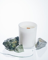 White candle of wax in a glass matte candlestick, next to it is a puddle of water and pebbles, symbolizing its fresh aroma