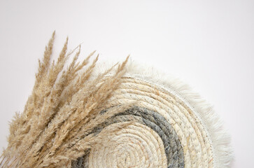 A round woven placemat, and dry spikelets on a light beige background.dry spikelets. Mock up. Concept of home comfort and interior elements.