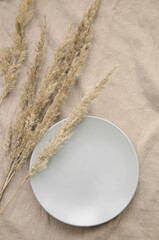 Ceramic plate with dried spikelets on a beige tablecloth. Eco natural concept. Mock up.