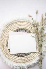 A round woven placemat, blank card and dry fluffy spikelets on a light beige background. Mock up. Concept of home comfort and interior elements. Restaurant promo. Buisness card.