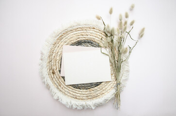 A round woven placemat, blank card and dry fluffy spikelets on a light beige background. Mock up. Concept of home comfort and interior elements. Restaurant promo. Buisness card.