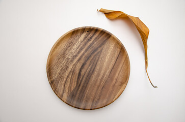 Round wooden craft plate mockup for eco, food or beauty product and dry aspidistra leaf on beige background. Top view. Copy space