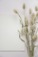White paper empty blank, dried flowers on beige background. Invitation card mockup on beige table. Flat lay, top view, copy space, mockup