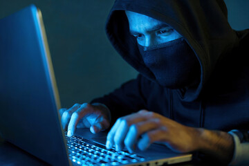 Hacker with his face covered sits at a laptop.