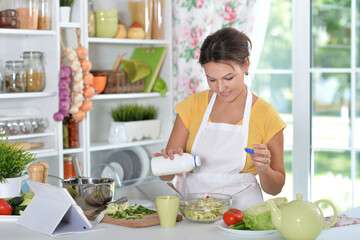 Naklejka premium Beautiful happy woman coocking salad on kitchen